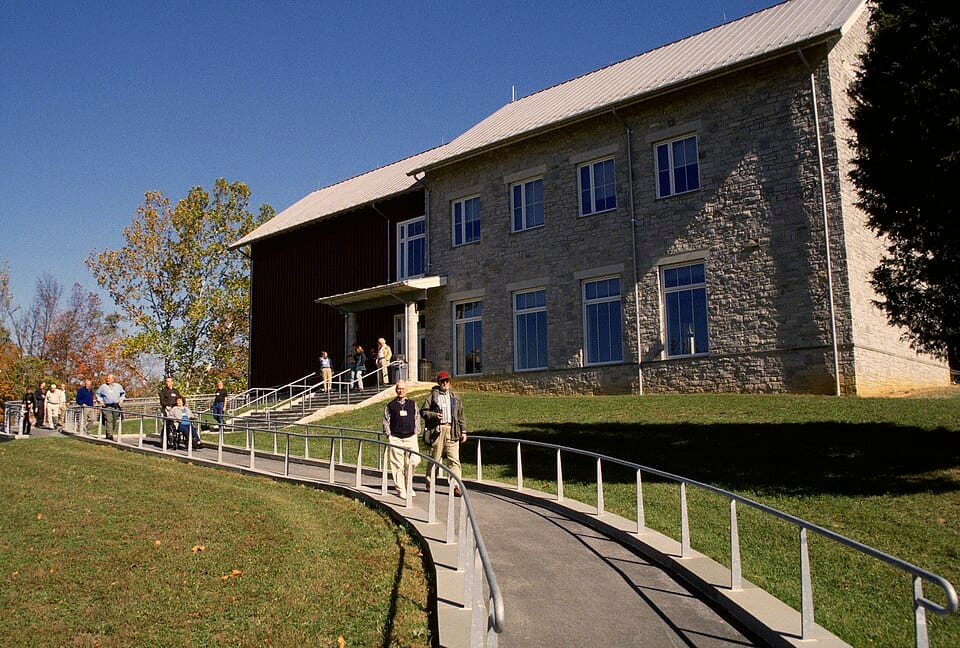 Visitors walking up a ramp toward a campus building on a sunny day.