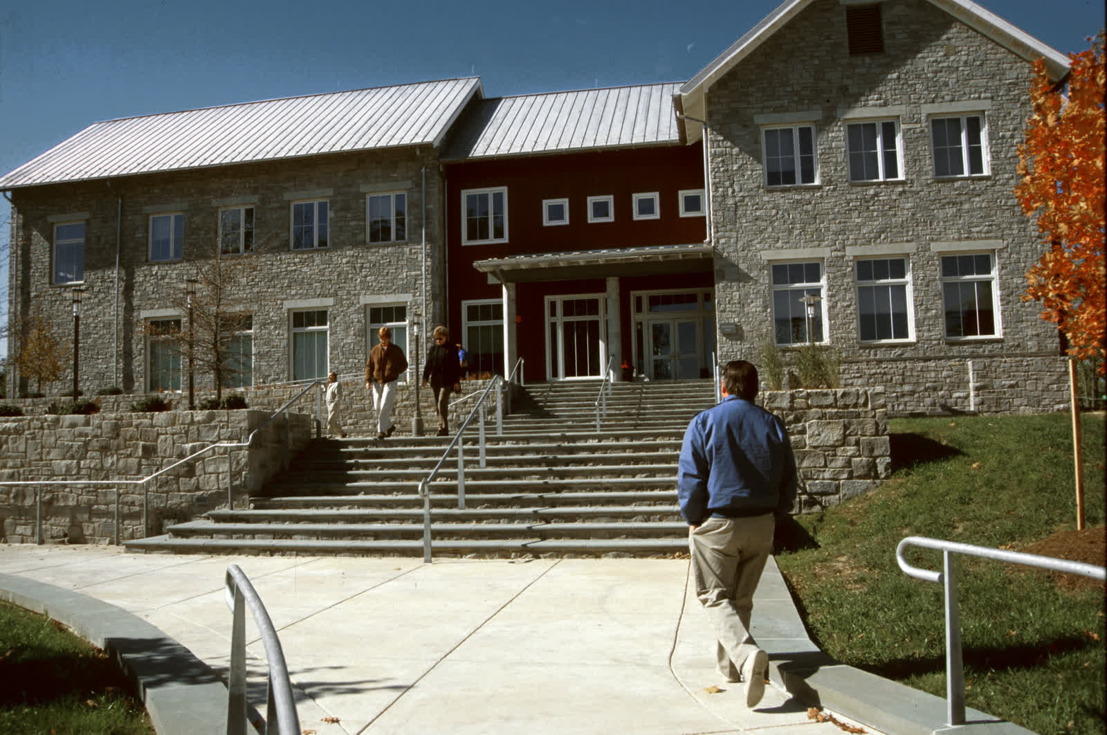 Students walking up stone steps to a campus building in autumn.