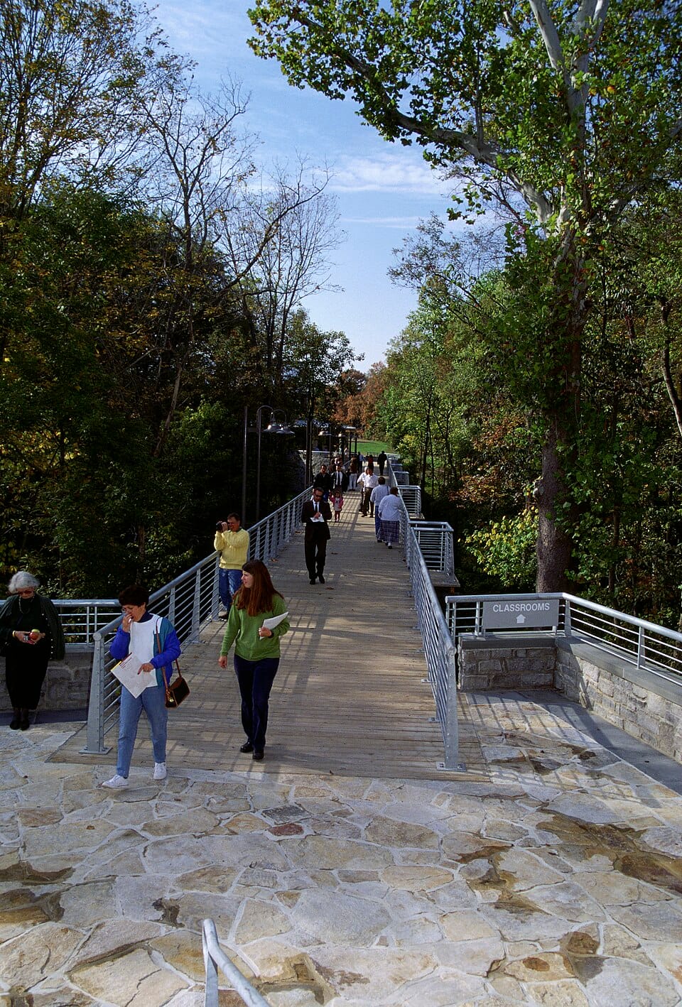 Visitors and students crossing a footbridge past a 