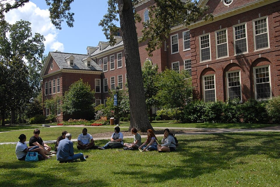 A group of students sitting together on the grass outside a campus building.